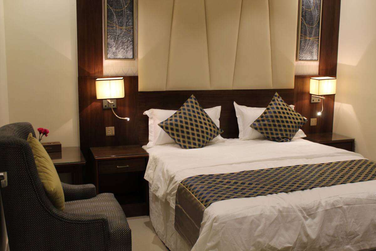 A hotel room with a large bed, two nightstands, a chair, and two wall-mounted lamps.
