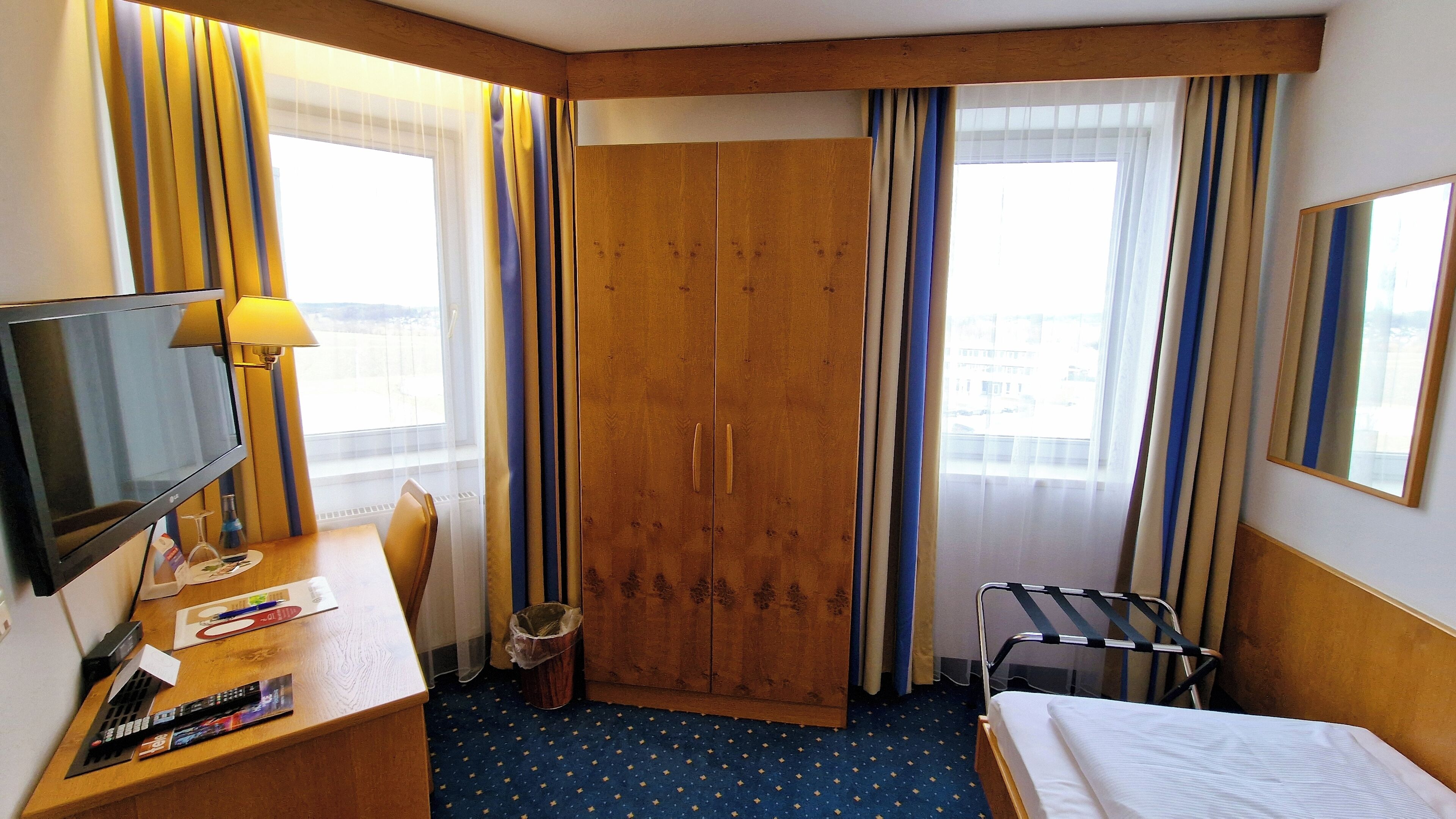 Ein Hotelzimmer mit Bett, Schreibtisch mit Fernseher, Stuhl, Kleiderschrank und einem Fenster mit Vorhängen.
