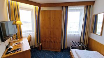 A hotel room with a bed, a desk with a TV, a chair, a wardrobe, and a window with curtains.
