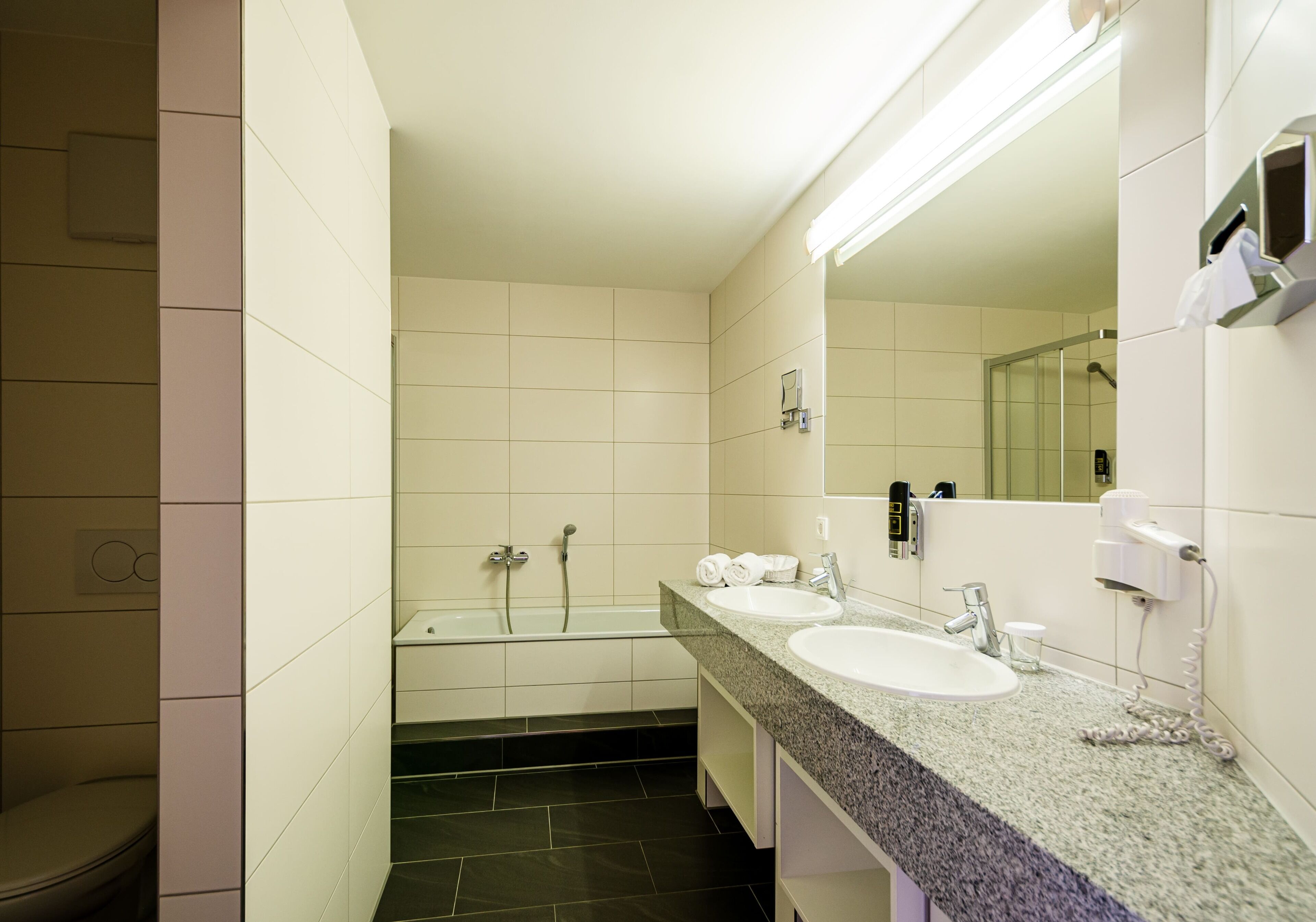 A modern bathroom with two sinks, a bathtub, and a toilet.