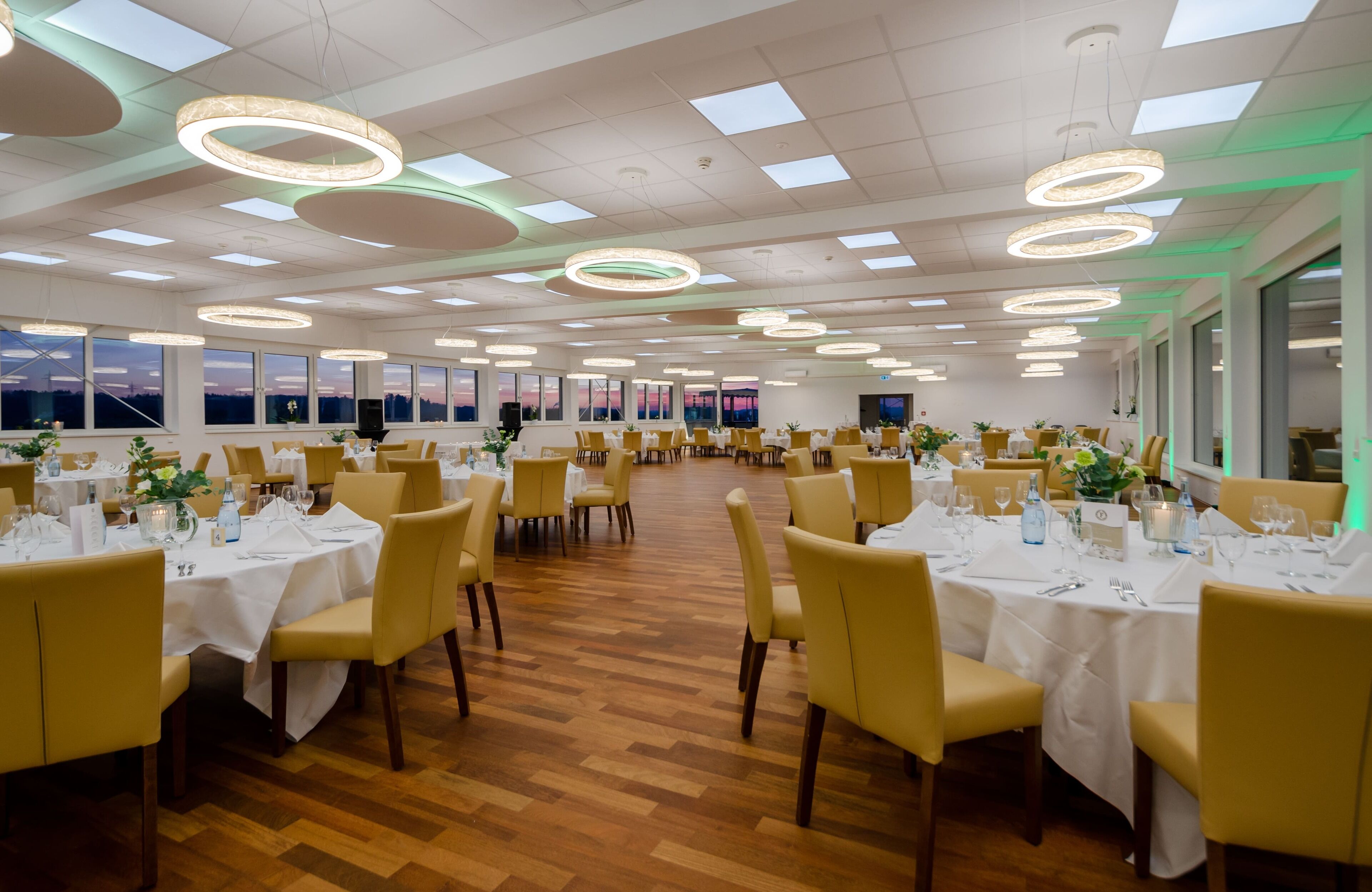 A spacious dining area with multiple round tables, chairs, and modern lighting fixtures.
