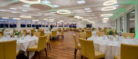 A spacious dining area with multiple round tables, chairs, and modern lighting fixtures.