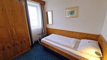 Une chambre d’hôtel avec un lit simple, une armoire, une fenêtre avec des rideaux et un tableau encadré au mur.