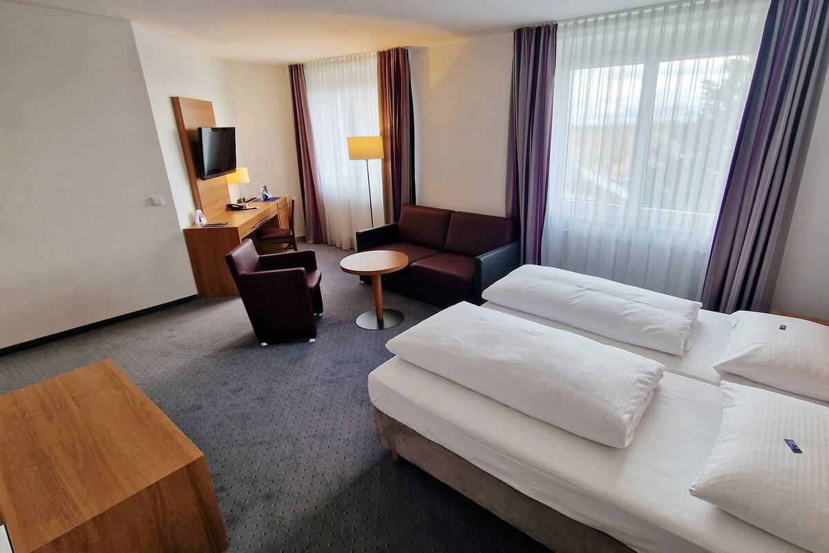 A hotel room with a bed, a desk, a chair, a sofa, and a TV.