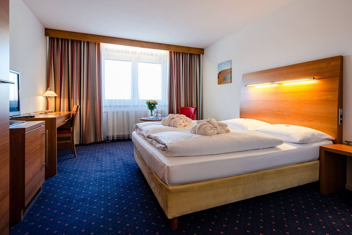 A hotel room with a bed, a desk, a chair, a TV, and a window with curtains.