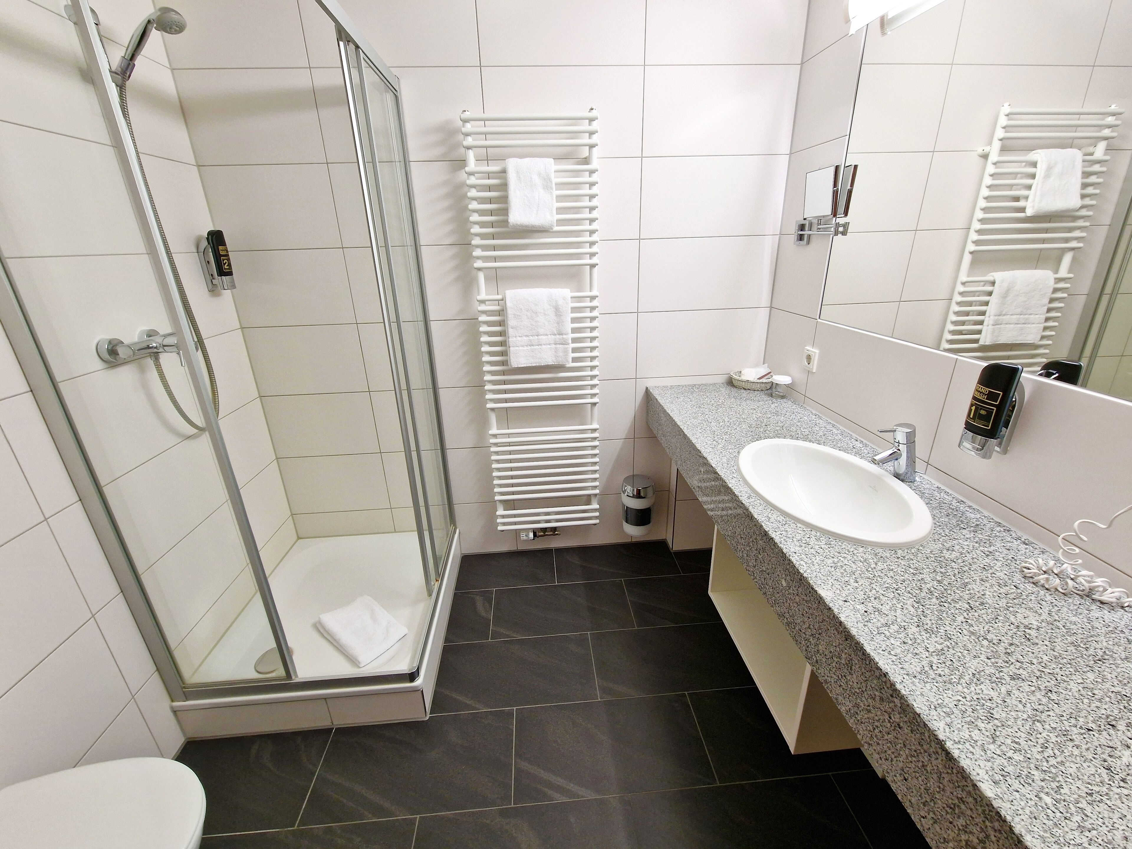 A modern bathroom with a glass-enclosed shower, a white sink, and a towel rack.