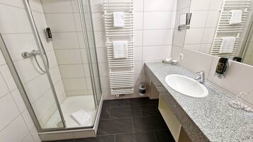 A modern bathroom with a glass-enclosed shower, a white sink, and a towel rack.