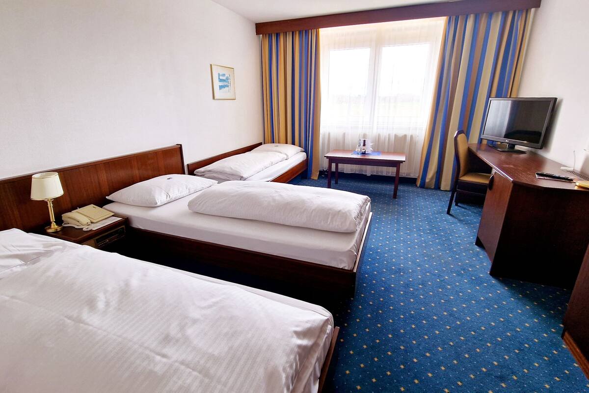 A hotel room with two single beds, a desk with a chair, a television, and a small table.
