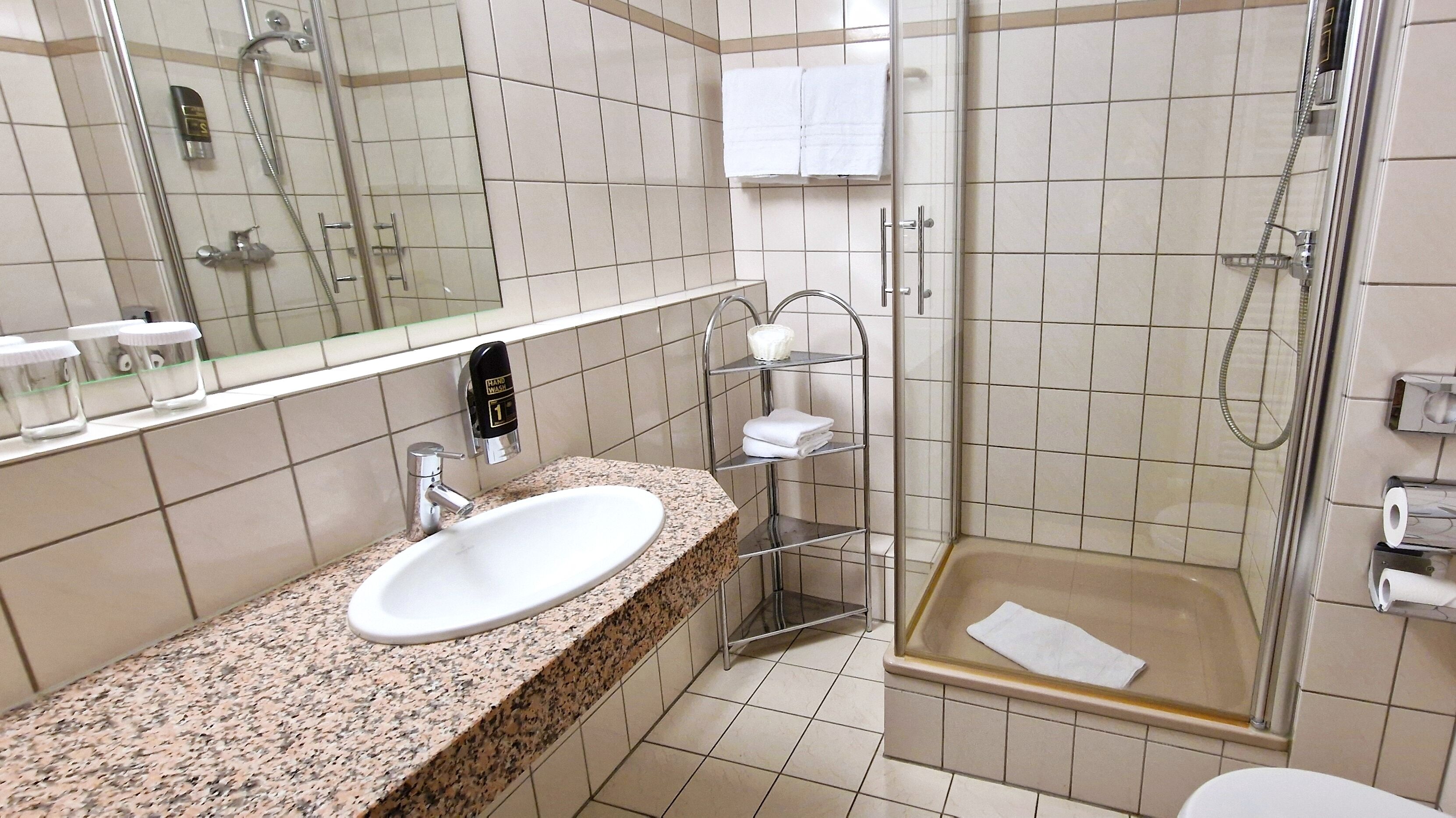A bathroom with a granite countertop sink, a glass shower enclosure, and a hand wash station.