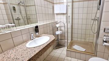 A bathroom with a granite countertop sink, a glass shower enclosure, and a hand wash station.