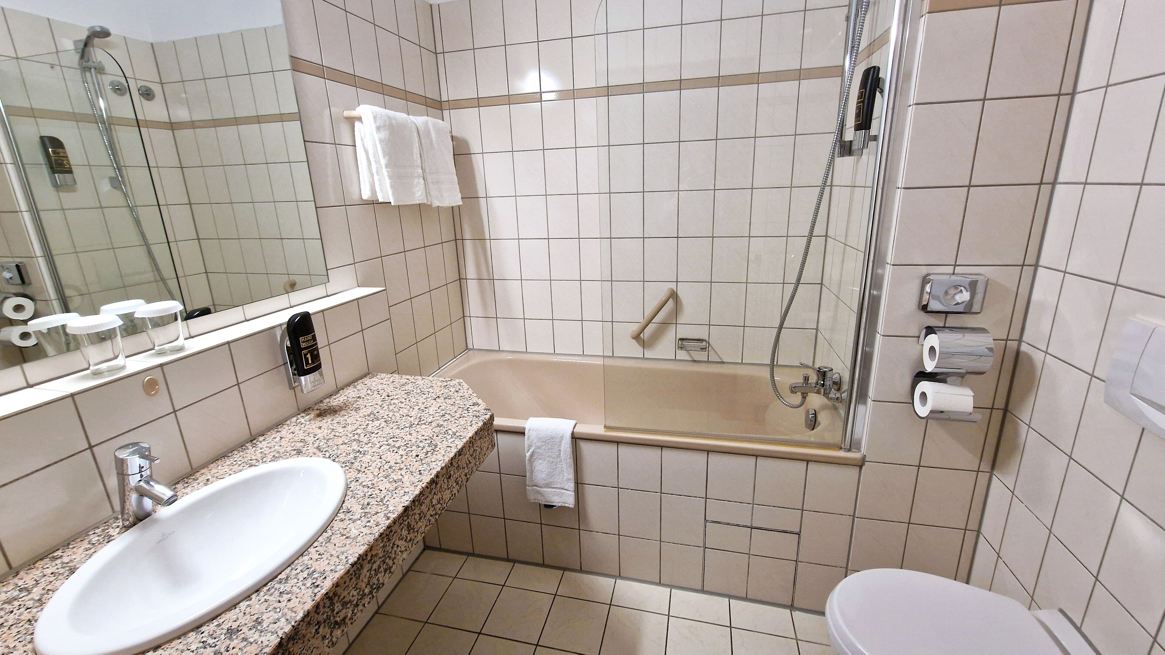 Een badkamer met een wastafel, spiegel, handdoekrek, douche en toilet.
