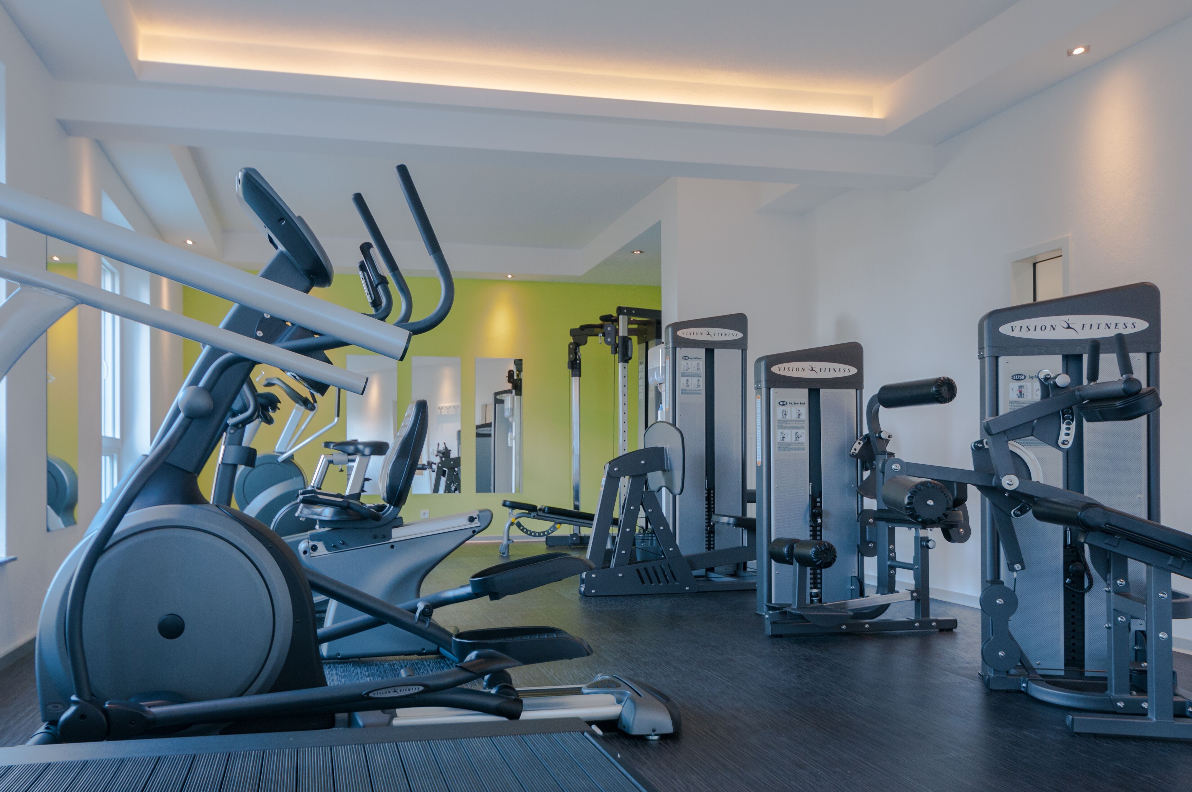 A gym with cardio machines, weight training equipment, and a mirrored wall.