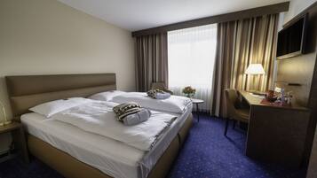A hotel room with a large bed, a desk, a chair, a TV, and a window with curtains.