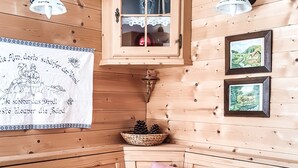 A cozy cabin interior with wooden walls, a wooden bench, a table with a red tablecloth, a cabinet, and two framed pictures. - Weigl Hütte (Semmering)