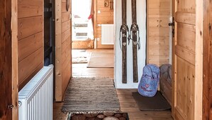 A wooden hallway with a patterned rug, a radiator, and skis leaning against the wall. - Weigl Hütte (Semmering)