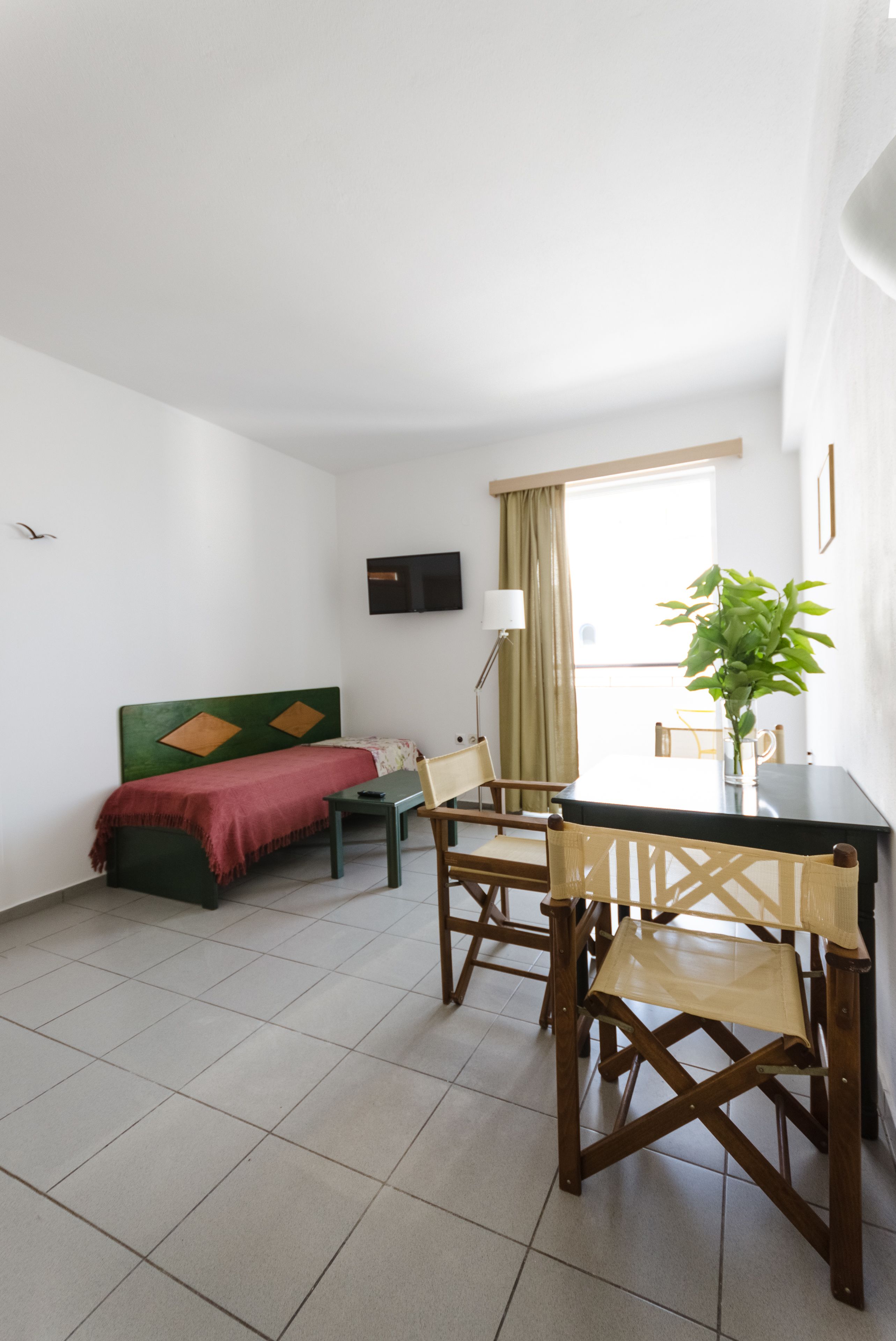 A room with a bed, a table with chairs, a lamp, and a plant.