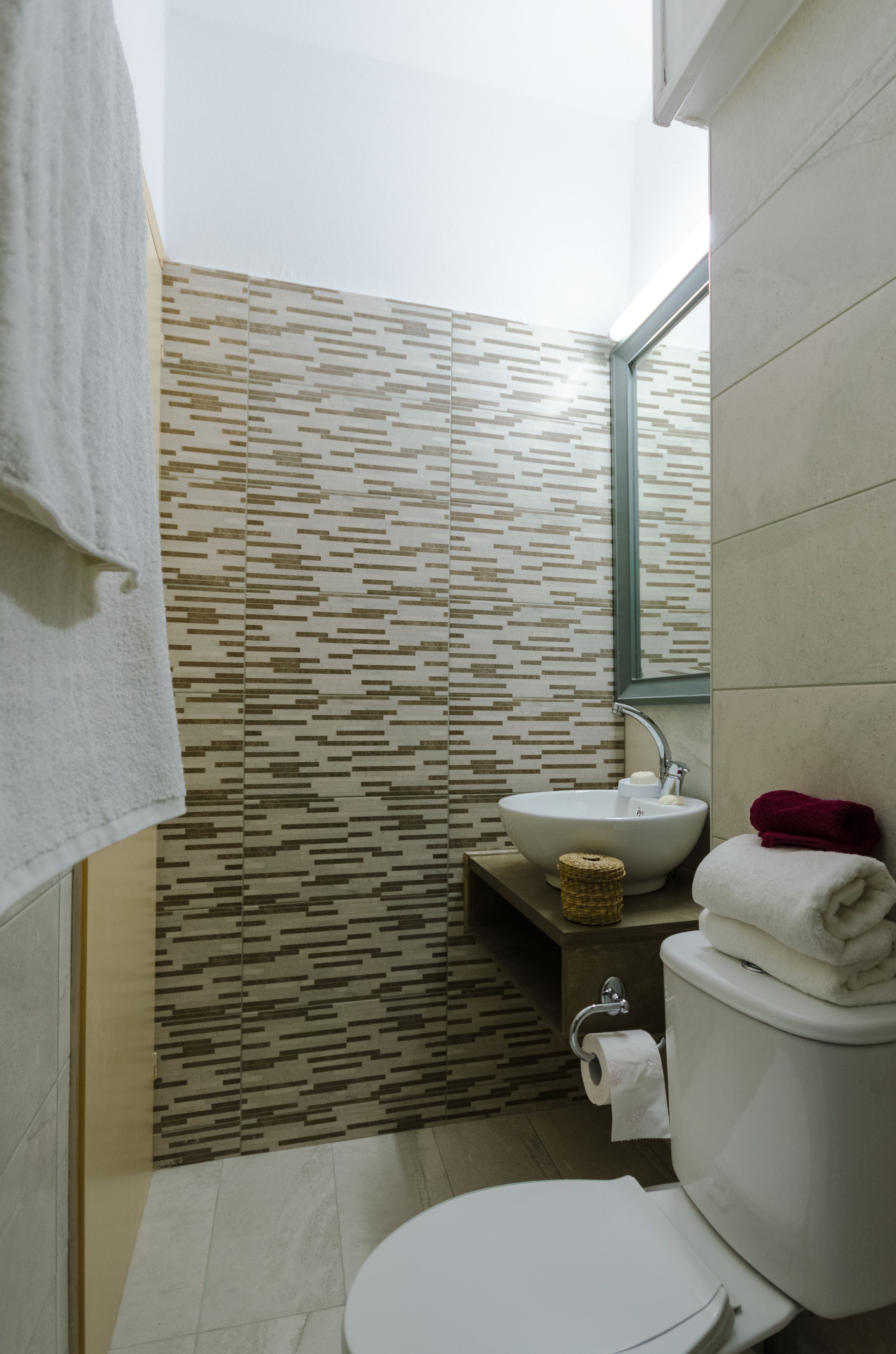 A compact bathroom with a patterned wall, a white sink, a toilet, and a mirror.