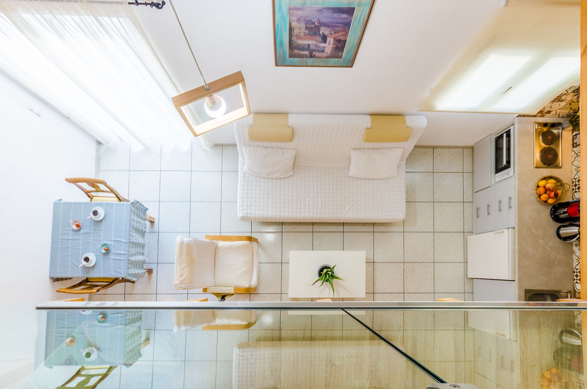 A modern bathroom with a glass shower enclosure, white tiled walls, a hanging light fixture, and a framed picture on the ceiling.