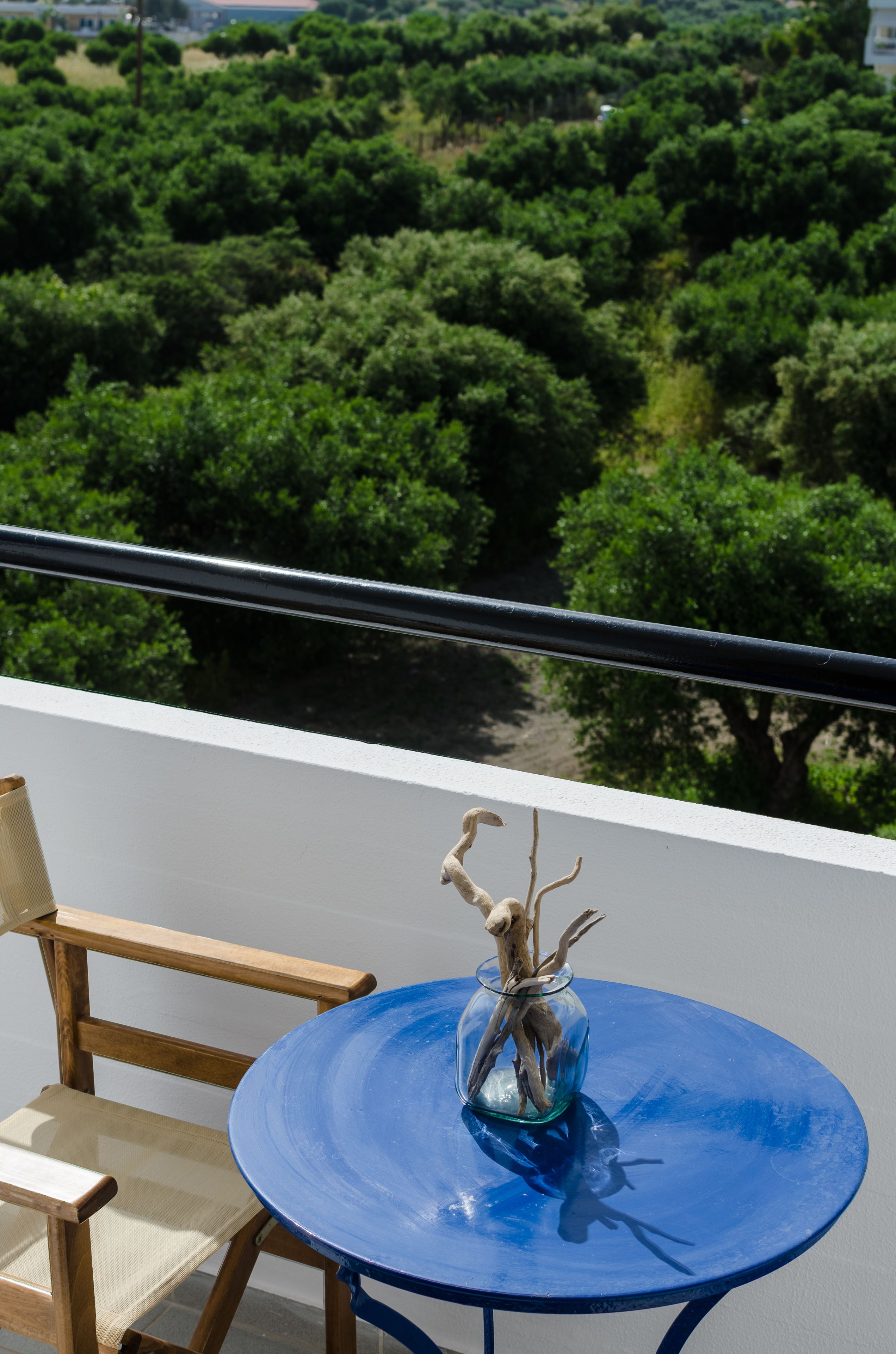 A balcony with a blue table and chairs, overlooking a dense green landscape.