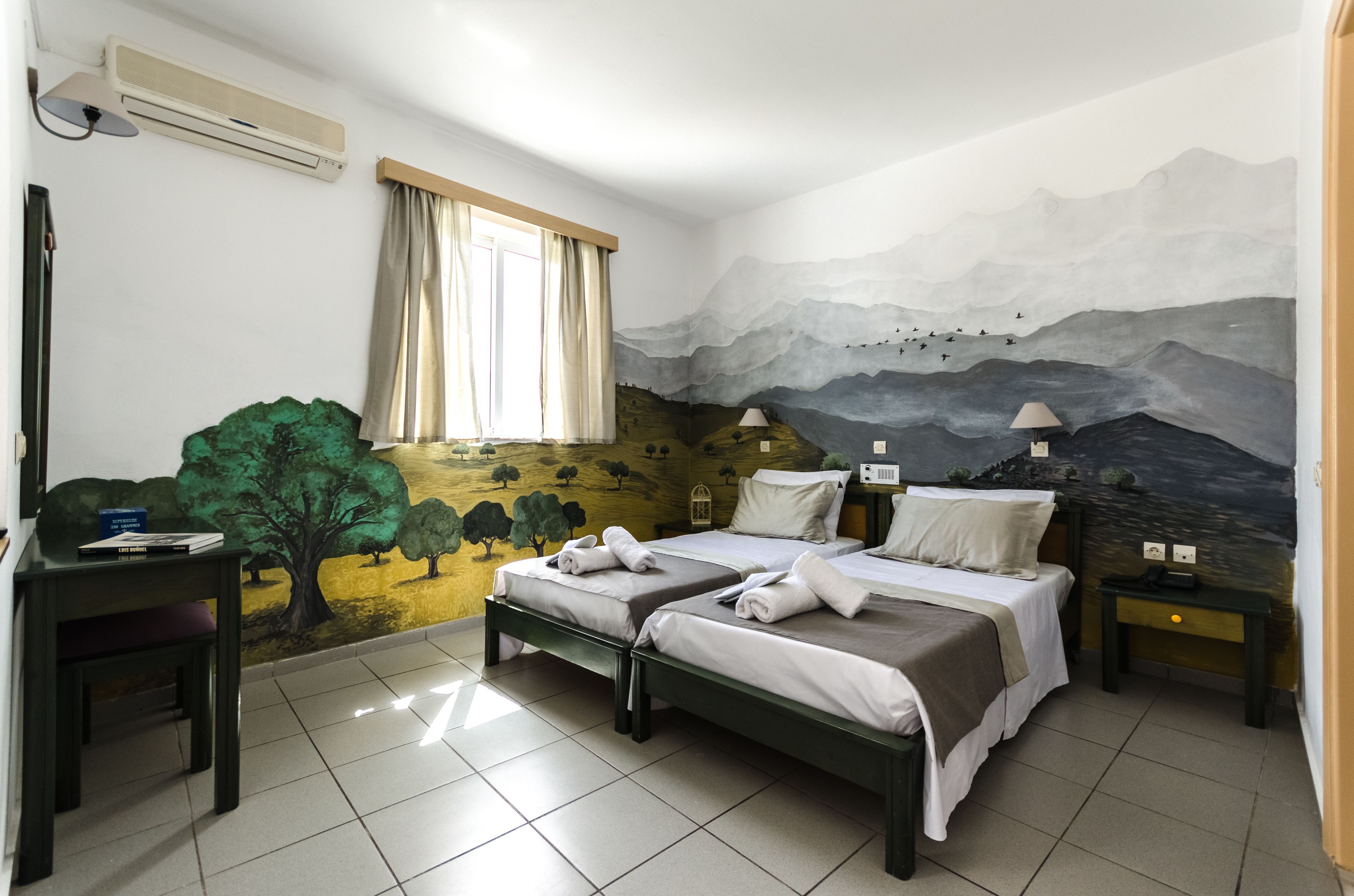 Habitación de hotel con dos camas, un escritorio y un mural en la pared.