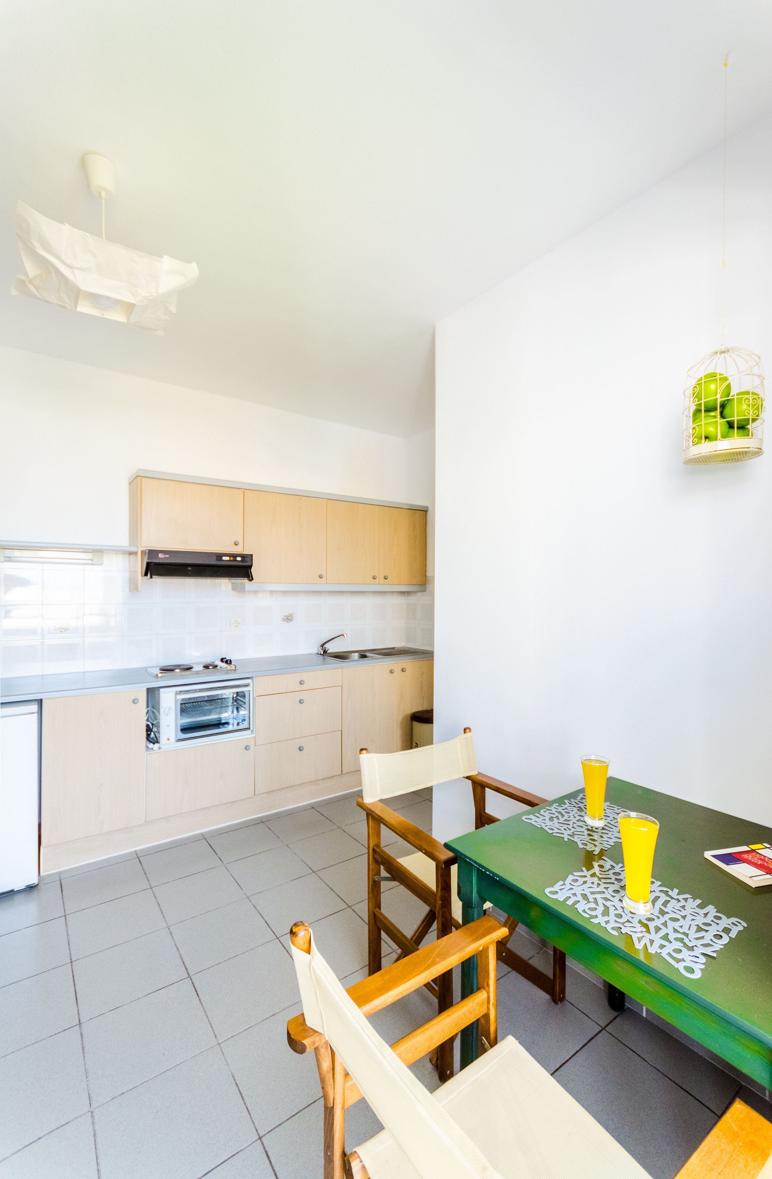 Une cuisine compacte dotée d’un four encastré, d’un évier et de meubles de rangement en bois. On y trouve une table à manger avec des chaises et un set de table vert.