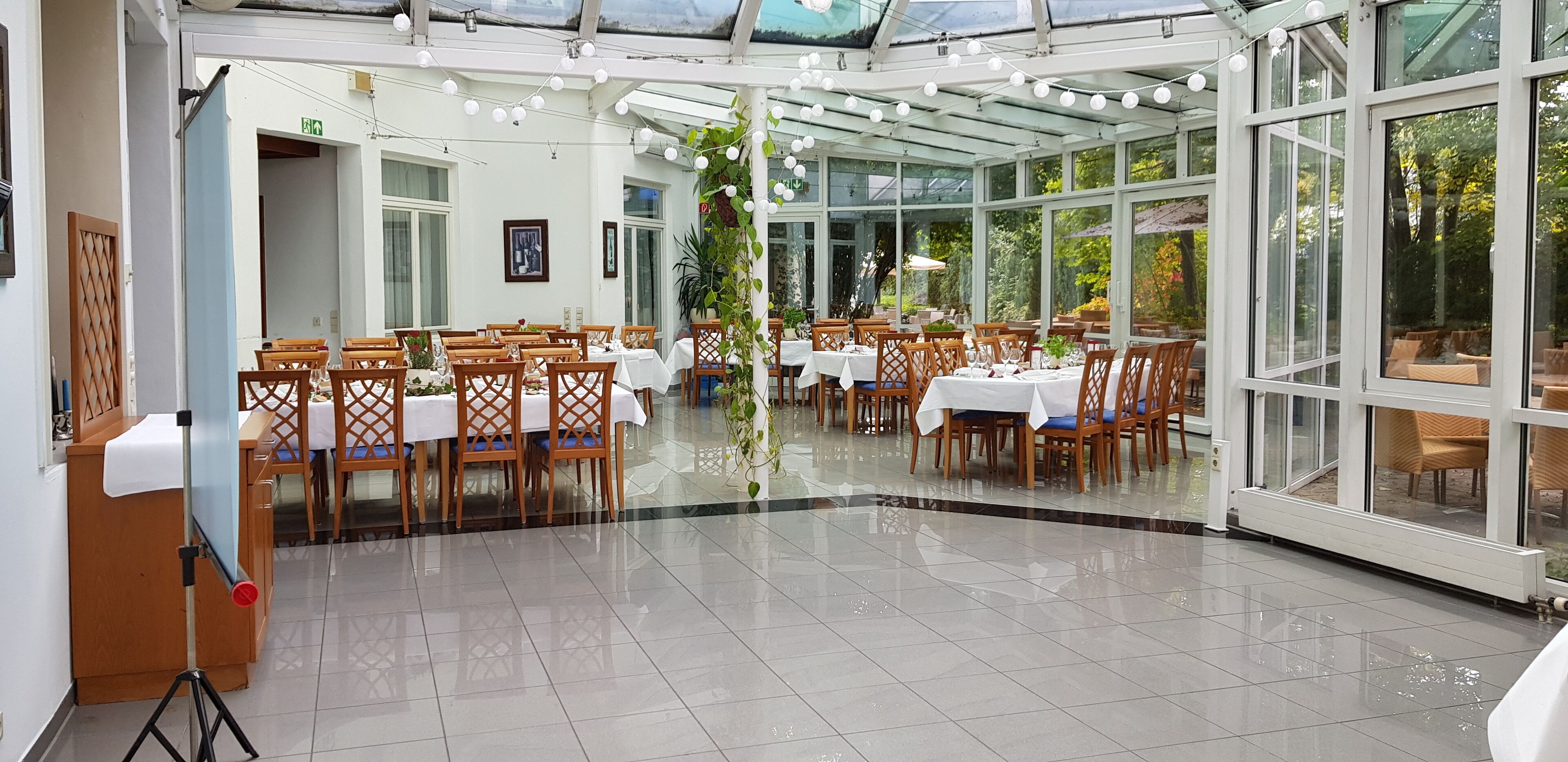 Un vaste espace intérieur aménagé en salle à manger, avec de nombreuses tables et chaises, de grandes fenêtres et un plafond en verre.