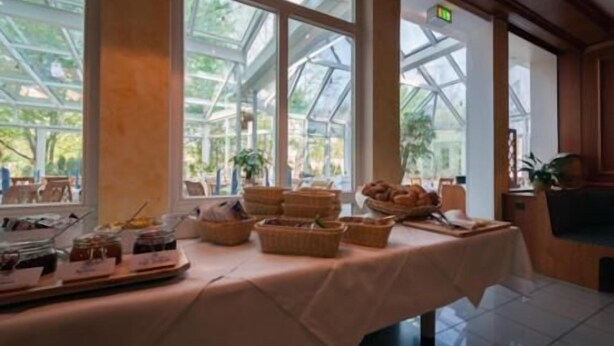 A breakfast buffet table with various food items and baskets, set in a room with large windows and a view of greenery outside. - Albhotel Fortuna (Riederich)