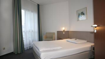 Habitación de hotel con una cama grande, una silla, una mesita de noche y una lámpara fijada a la pared.