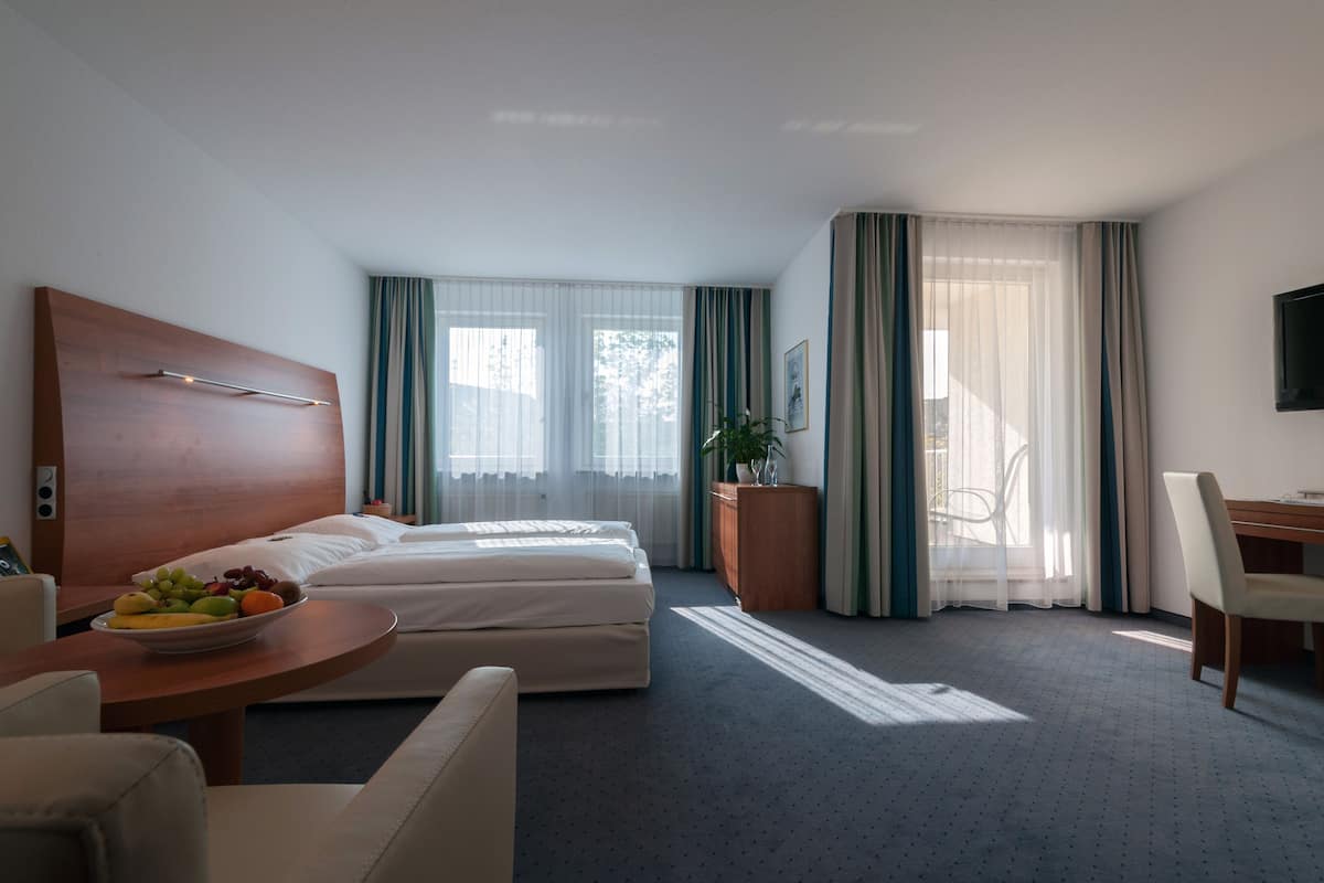 A hotel room with a bed, a desk, a chair, a TV, and a bowl of fruit.