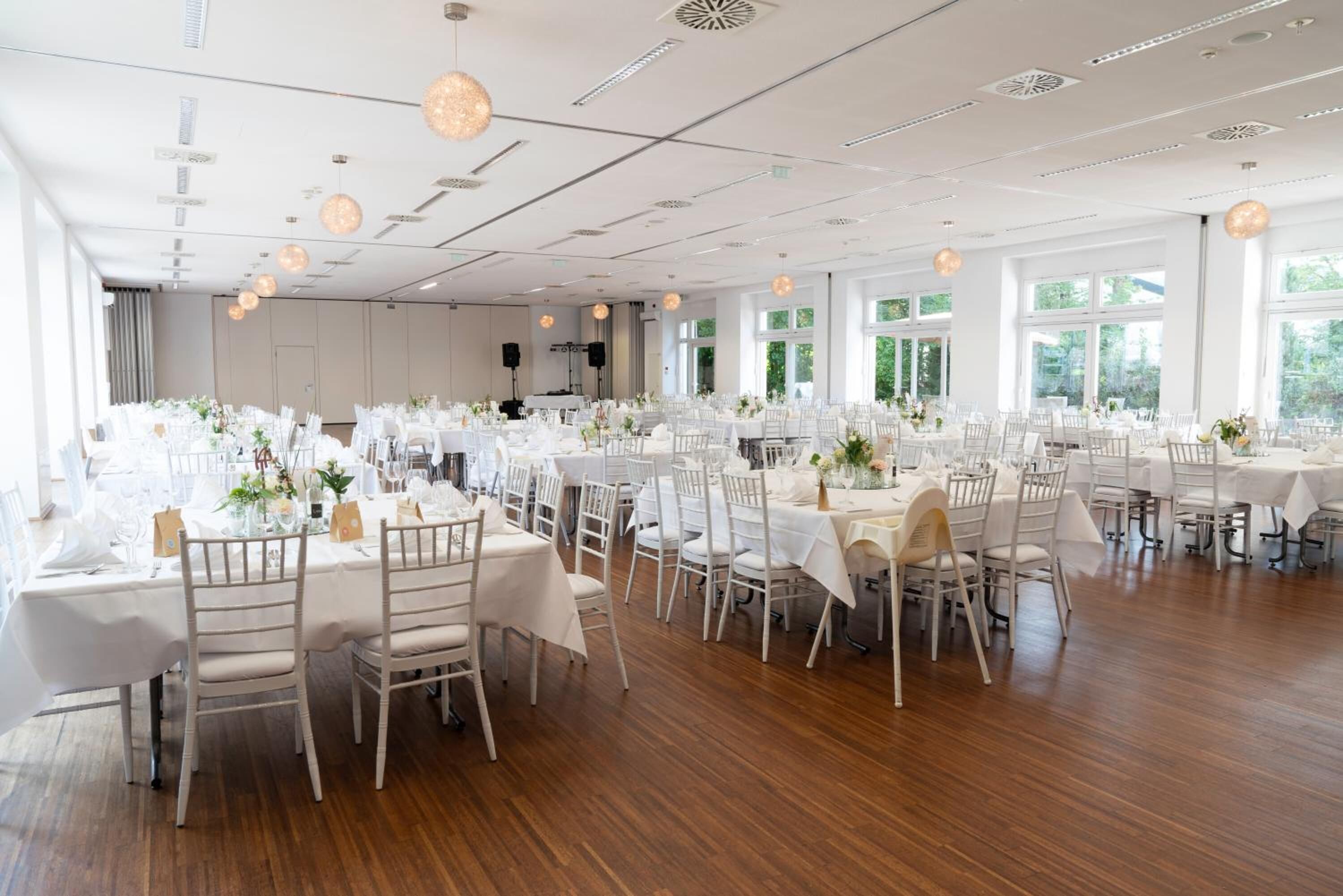 Ein geräumiger Festsaal mit mehreren runden Tischen, die mit weißen Tischdecken bedeckt und in Reihen angeordnet sind.