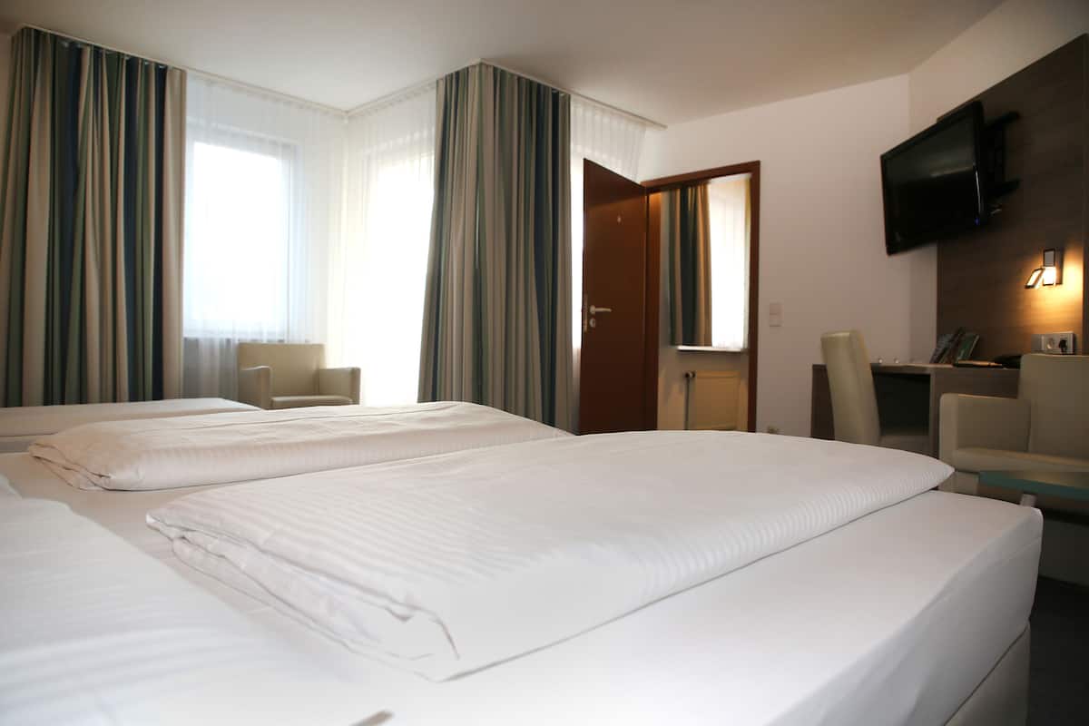 A hotel room with two beds, a desk, a chair, a television, and a door.