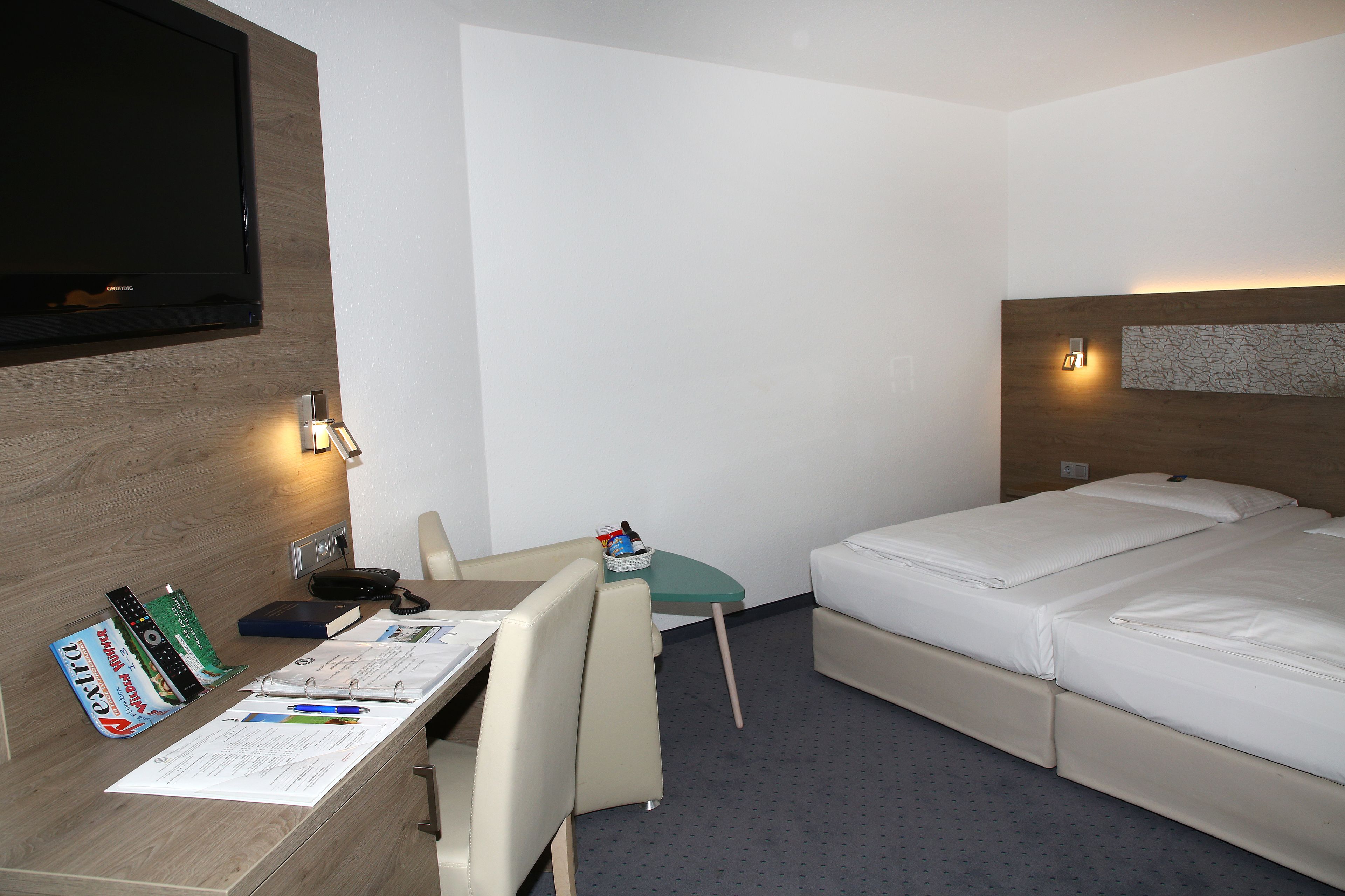 Et hotelværelse med seng, skrivebord med stol, fjernsyn og et lille bord med lampe.