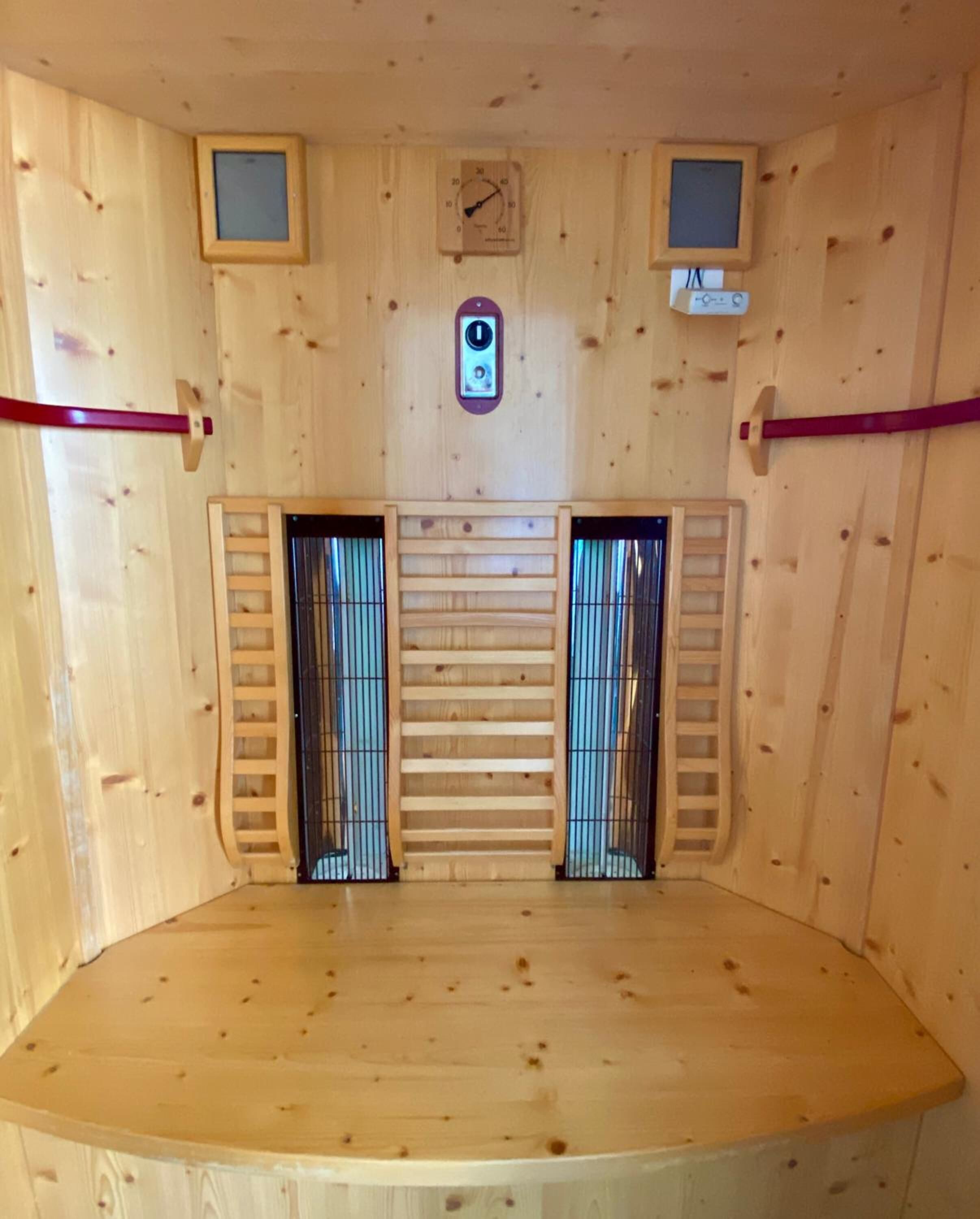 A sauna room with wooden walls, a central bench, two small windows, and a wall-mounted clock.