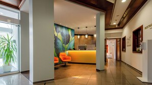 A reception area with a modern design, featuring a reception desk, a colorful abstract mural, and a seating area with orange chairs. - Albhotel Fortuna (Riederich)