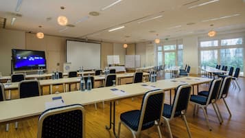 A conference room with long tables, chairs, a projector screen, and a whiteboard.
