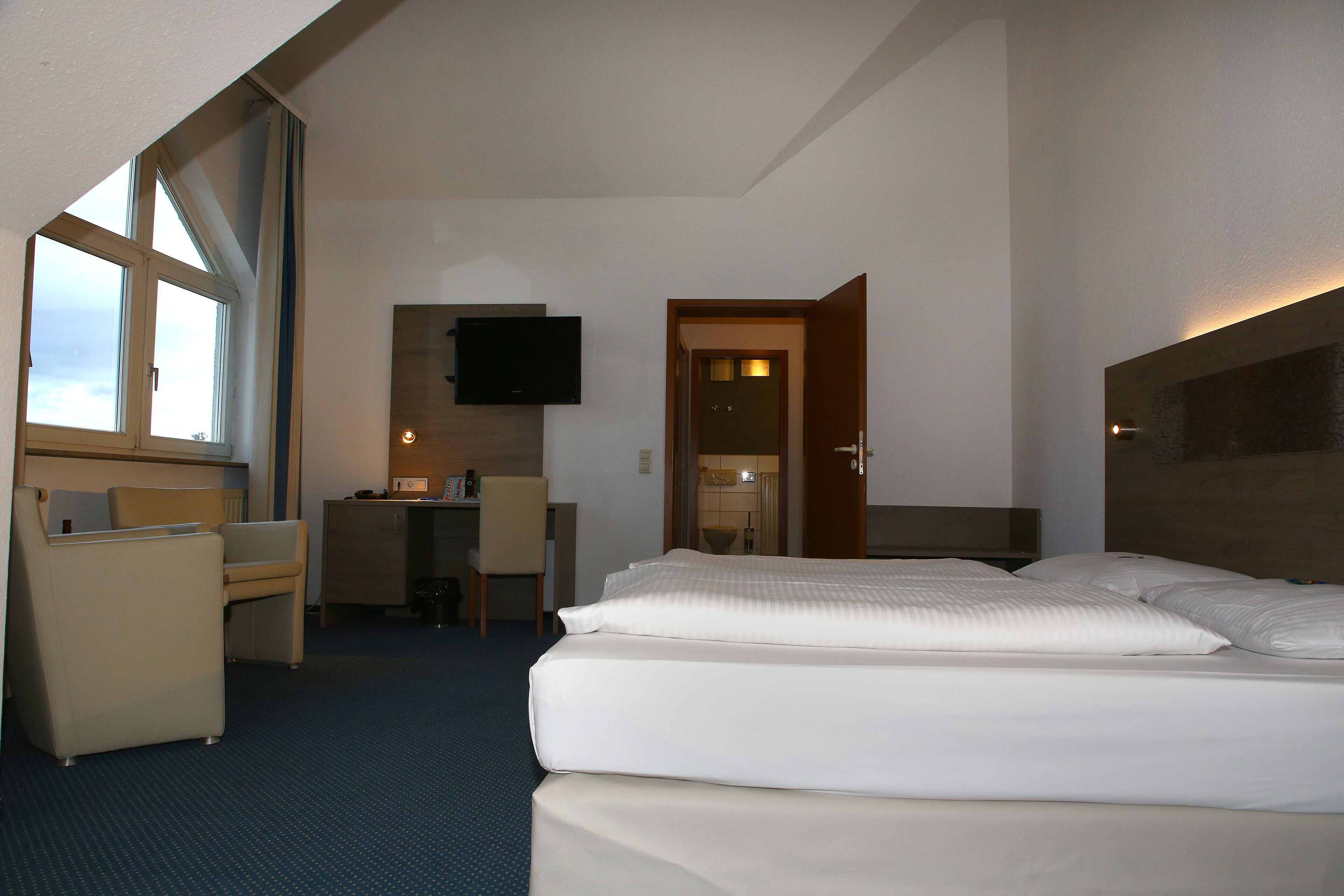 A hotel room with a large bed, a desk, a chair, and a TV mounted on the wall.