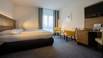 Ein Hotelzimmer mit Bett, Schreibtisch, Stuhl, Fernseher und einem Fenster mit Vorhängen.
