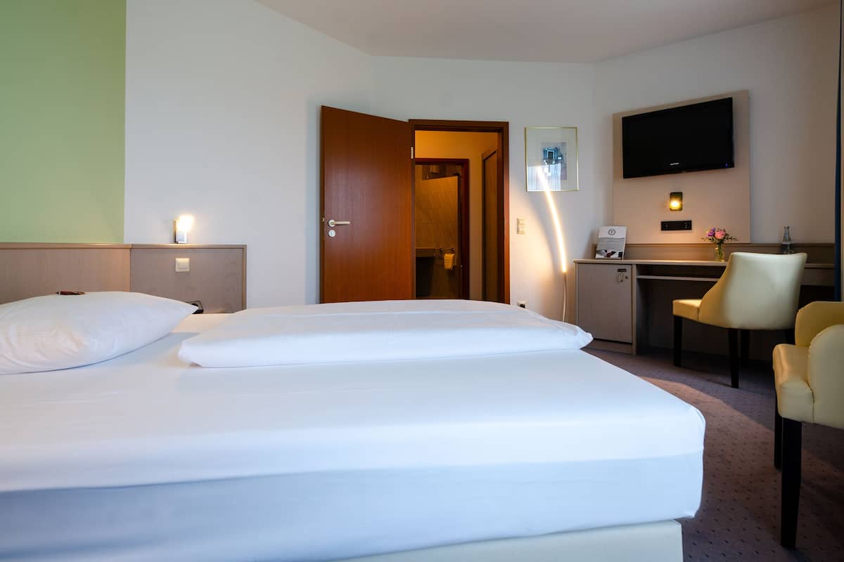 A hotel room with a bed, a desk, a chair, and a television.