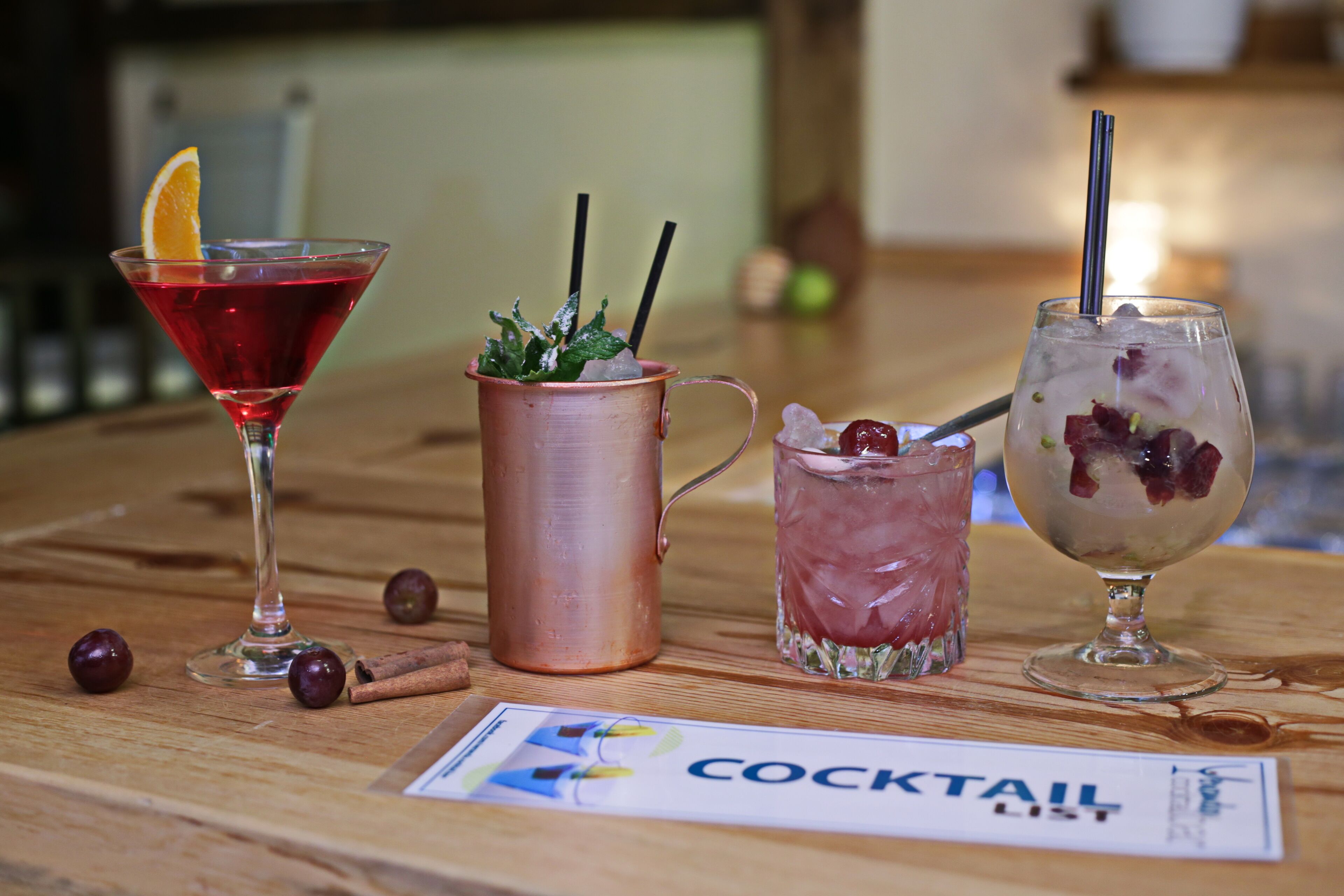 Three cocktails on a wooden table with a cocktail menu.