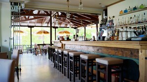 A bar area with wooden stools, a bar counter, and a variety of bottles and glasses. - Hotel Magdalena (Kassandra)