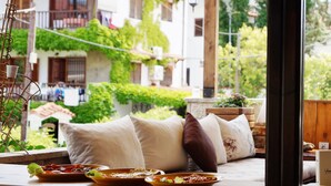 A cozy seating area with a view of a garden and buildings, featuring a table with plates of food and a window with a view of a balcony. - Hotel Magdalena (Kassandra)