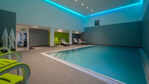 An indoor swimming pool with a blue-lit ceiling, a changing room with green chairs, and a seating area with white chairs. - Hotel Fortuna (Schwaebisch Gmuend)