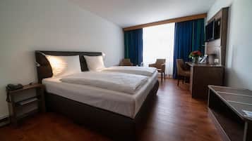 Een hotelkamer met een groot bed, nachtkastjes, een bureau met stoel, een televisie en een raam met gordijnen.