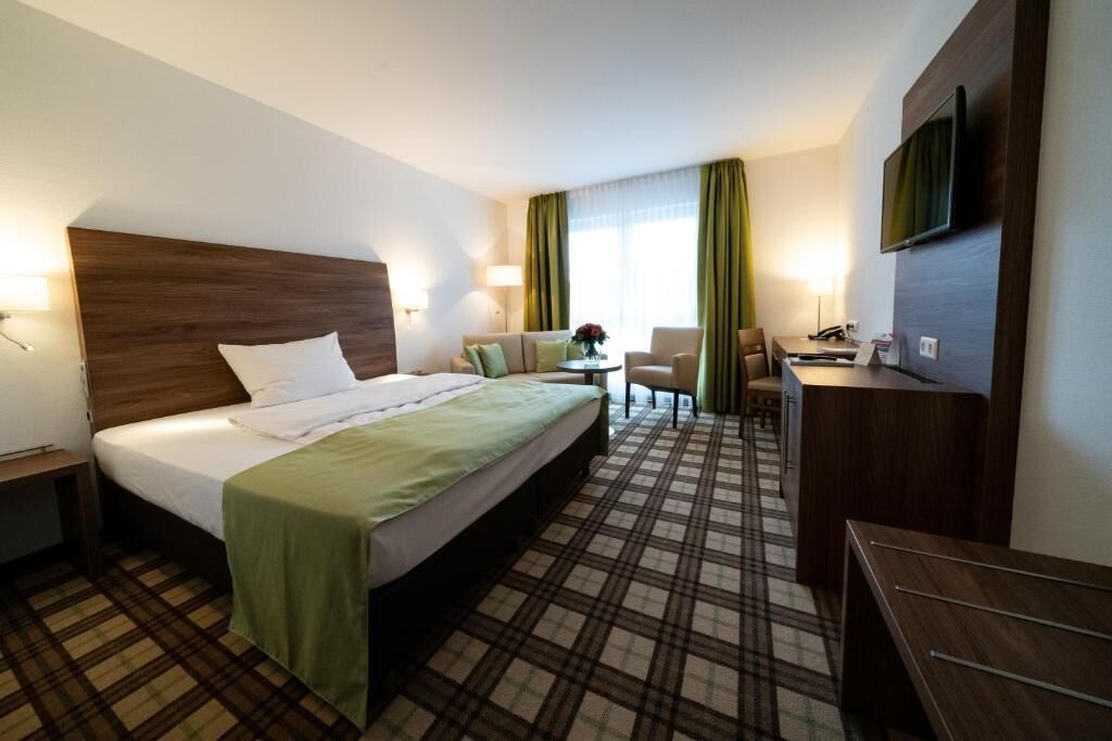 Una habitación de hotel con cama, escritorio, silla, televisor y ventana con cortinas.