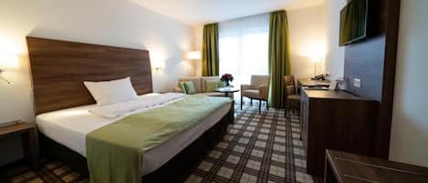 Une chambre d’hôtel avec un lit, un bureau, une chaise, une télévision et une fenêtre avec des rideaux.