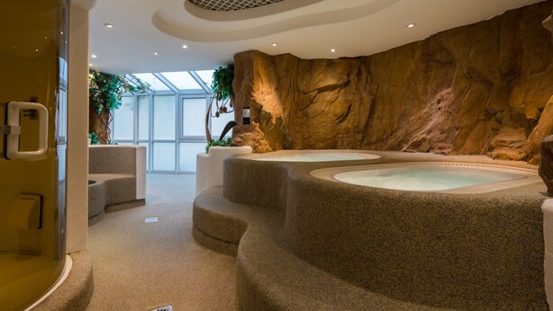 A spa area with two hot tubs, a rock wall, and a glass door leading to a room. - Hotel Fortuna (Schwaebisch Gmuend)