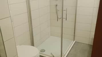 Un baño con ducha de vidrio, inodoro y piso de baldosas.