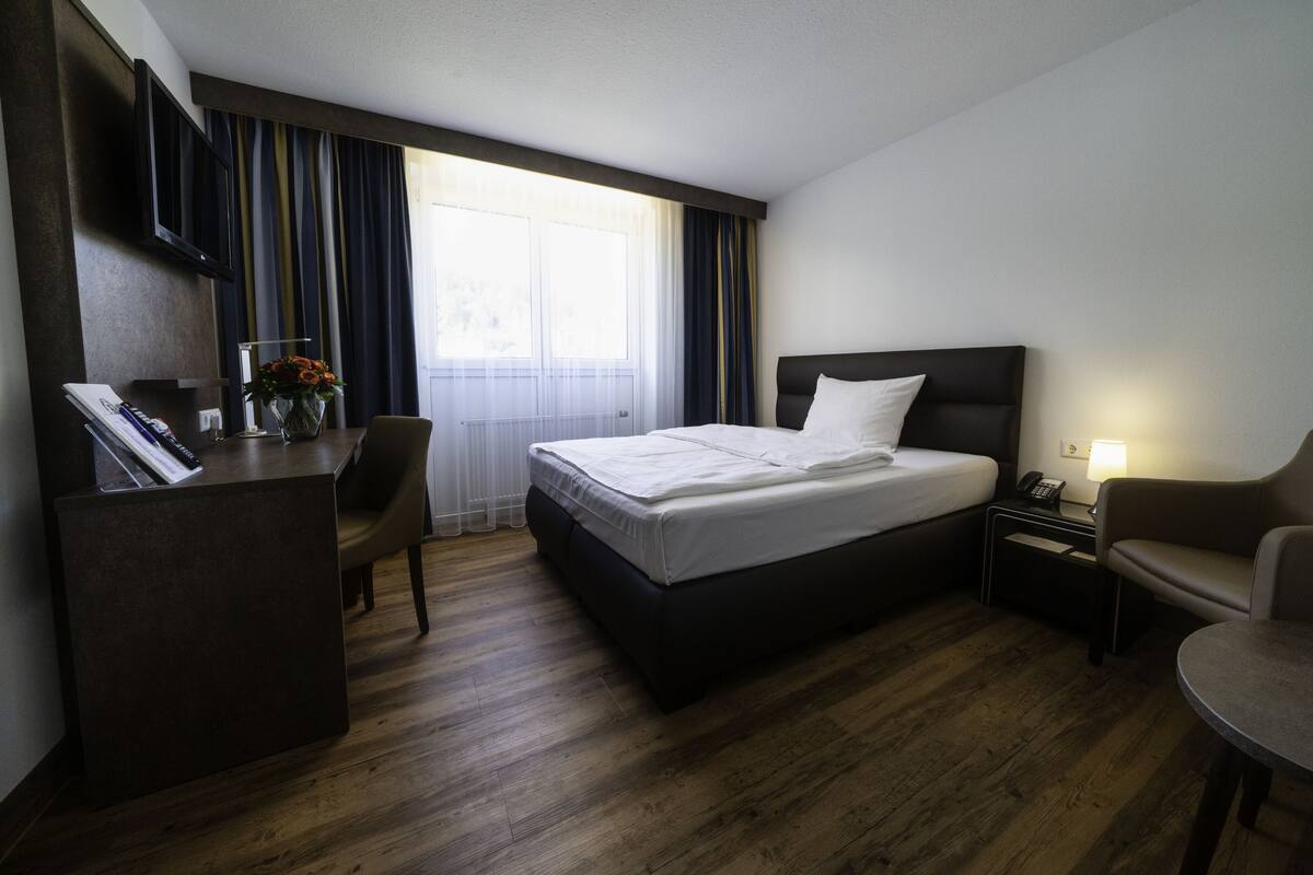 A hotel room with a bed, desk, chair, and a small table.