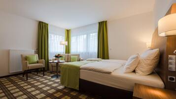 Una habitación de hotel con una cama, una silla, una mesita con lámpara y una ventana con cortinas.