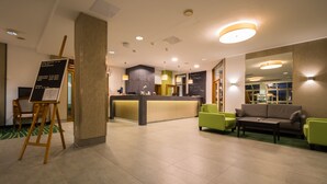 A hotel lobby with a reception desk, seating area, and a green carpet. - Hotel Fortuna (Schwaebisch Gmuend)